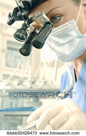 Stock Image - "Dentist, dental hygienist, wearing a face mask and magnifying loupes". Fotosearch