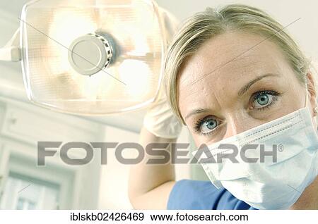 "Dentist, dental hygienist, wearing a face mask and adjusting a dentist's lamp" View Large Photo Image Stock Photo - "Dentist, dental hygienist, wearing a face mask and adjusting a dentist's lamp". Fotosearch