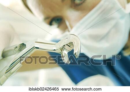 Dentist wearing a face mask and holding dental pliers for pulling teeth View Large Photo Image Stock Photography - Dentist wearing a face mask and holding dental pliers for pulling teeth. Fotosearch