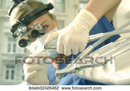 Stock Image - Dentist wearing magnifying loupes preparing a drill. Fotosearch