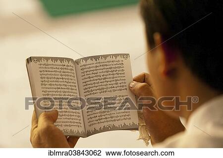 Stock Image - "Devout Buddhist reading holy scripture, from behind, Yangon, Myanmar, Asia". Fotosearch