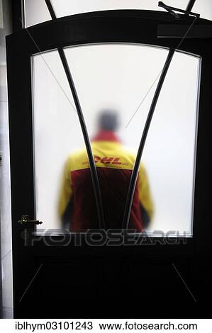 Stock Image - "DHL parcels delivery driver is standing in front of a front door with frosted glass, Germany, Europe". Fotosearch