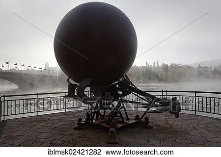 Stock Image - Dickfigur Beteigeuze sculpture by Swiss artist Bernhard Luginbuehl in the morning mist, on a concrete base on the German shore of the Rhine river, Rheinfelden - Baden, Baden-Wuerttemberg, Germany, Europe. Fotosearch