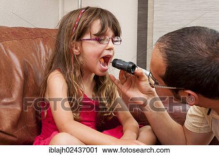 Stock Image - Doctor during a home visit examining a girl with an otoscope. Fotosearch