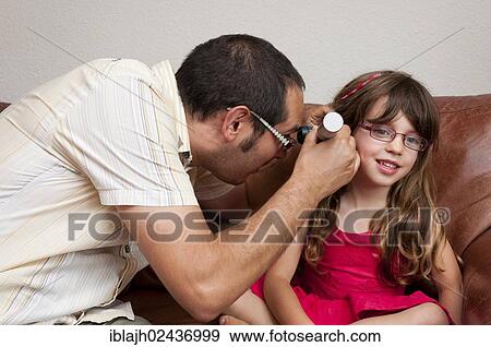 Doctor on a home visit examining a girl with an otoscope View Large Photo Image Stock Photo - Doctor on a home visit examining a girl with an otoscope. Fotosearch