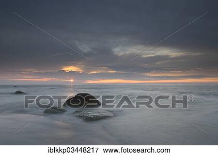 Stock Photo - "Dramatic cloudy sky at sunset, stones on the beach, Dranske, Mecklenburg-Western Pomerania, Germany, Europe". Fotosearch