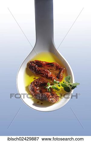 Stock Photo - Dried tomatoes in olive oil on a white spoon. Fotosearch