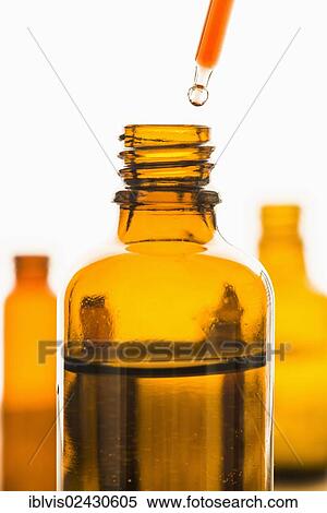 Stock Photography - Dropper with red substance held over transparent brown bottle. Fotosearch