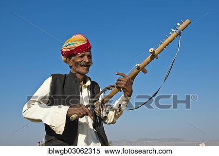 Stock Photography - "Elderly friendly Indian man, Rajasthani, wearing a colourful turban and playing on a sitar, Kamelmarkt Pushkar, Pushkar, Wuste Thar, Rajasthan, India, Asia". Fotosearch