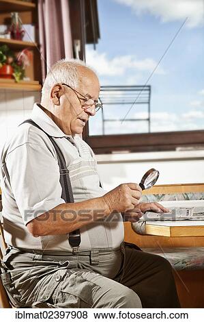 Stock Photo - Elderly man reading a newspaper with a magnifying glass. Fotosearch