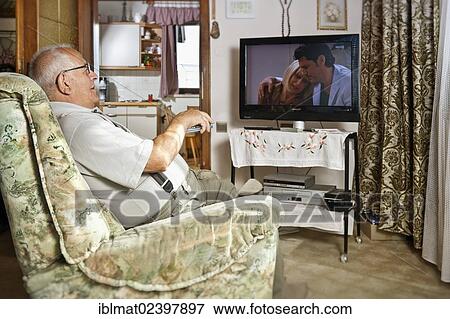 Elderly man sitting in front of a TV operating a remote control View Large Photo Image Stock Photo - Elderly man sitting in front of a TV operating a remote control. Fotosearch