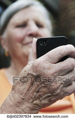 Picture - Elderly woman holding a smartphone in her hand. Fotosearch
