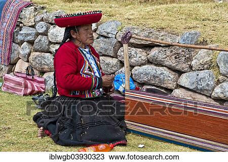 Stock Image - "Elderly woman wearing a hat, Quechua Indian in a traditional dress, sitting on the floor and working on a stretcher of a loom, Cinchero, Urubamba Valley, Peru, South America". Fotosearch