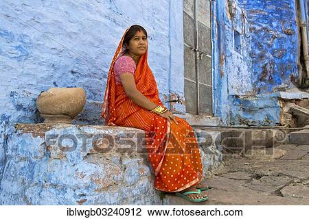 "Elderly woman wearing a red sari sitting on a ledge of a blue painted residential building, Brahmpuri, Jodhpur, Rajasthan, India, Asia" View Large Photo Image Stock Image - "Elderly woman wearing a red sari sitting on a ledge of a blue painted residential building, Brahmpuri, Jodhpur, Rajasthan, India, Asia". Fotosearch