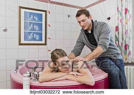 Stock Image - "Expectant father massaging his wife's shoulders during childbirth in a birthing bath, Germany, Europe". Fotosearch