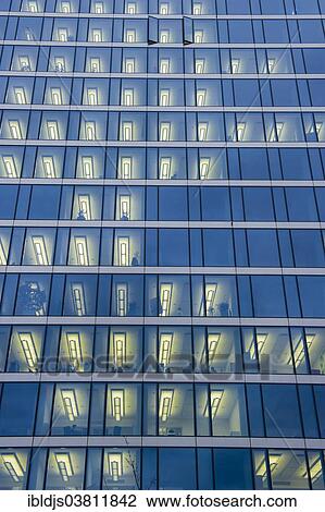 Stock Image - "Facade of a modern office building with lights on in the offices in the evening, Munich, Bavaria, Germany, Europe". Fotosearch