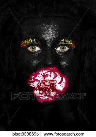 "Face of a young woman painted with black facepaint, with multi-coloured eyelashes and a flower in her mouth, Austria, Europe" View Large Photo Image Stock Image - "Face of a young woman painted with black facepaint, with multi-coloured eyelashes and a flower in her mouth, Austria, Europe". Fotosearch