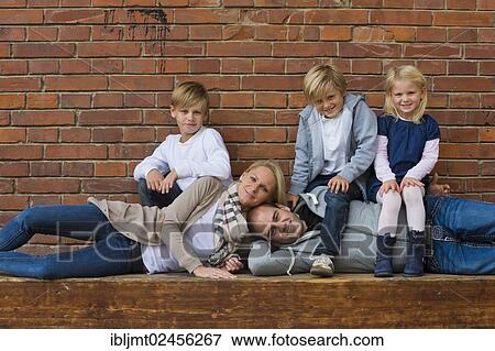 "Family portrait with three children, the parents are lying, the children are sitting on them" View Large Photo Image Stock Photo - "Family portrait with three children, the parents are lying, the children are sitting on them". Fotosearch