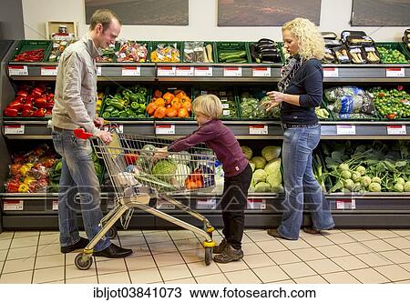 Stock Image - "Family shopping with a shopping trolley in the fruit and vegetables department of a supermarket, Germany, Europe". Fotosearch