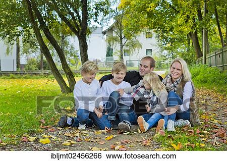 Family with three children sitting on a meadow with autumn leaves View Large Photo Image Stock Photograph - Family with three children sitting on a meadow with autumn leaves. Fotosearch
