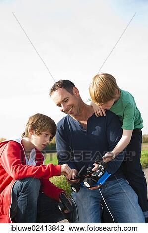 Stock Image - Father tinkering on a remote-controlled model car with his sons. Fotosearch