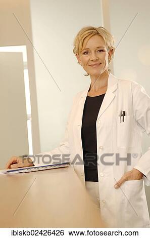 Female doctor in a white coat is standing at a reception desk View Large Photo Image Stock Photograph - Female doctor in a white coat is standing at a reception desk. Fotosearch