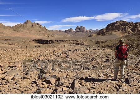 Stock Image - "Female hiker standing in the volcanic landscape at Atakor, Hoggar Mountains, Atakor, Tamanrasset Province, Algeria, Africa". Fotosearch
