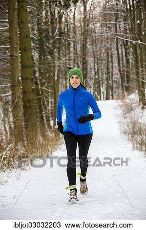 Stock Image - "Female jogger on a run in a snow-covered forest, in winter". Fotosearch