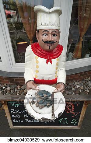 "Figure of a chef holding a plate with a fish dish outside a restaurant, Zingst, Darss, Mecklenburg-Western Pomerania, Germany, Europe" View Large Photo Image Stock Photo - "Figure of a chef holding a plate with a fish dish outside a restaurant, Zingst, Darss, Mecklenburg-Western Pomerania, Germany, Europe". Fotosearch