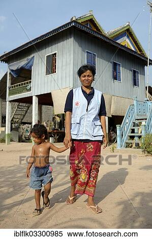 "First aid and community health worker wearing a vest of the Red Cross, holding a young girl's hand in front of a traditional house, Tropeng Village, Bathi District, Takeo Province, Cambodia, Asia" View Large Photo Image Stock Photography - "First aid and community health worker wearing a vest of the Red Cross, holding a young girl's hand in front of a traditional house, Tropeng Village, Bathi District, Takeo Province, Cambodia, Asia". Fotosearch