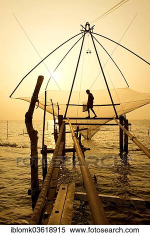 Stock Photography - "Fisherman holding a landing net in a Chinese fishing net at sunrise, Vembanad lake, Kerala, India, Asia". Fotosearch