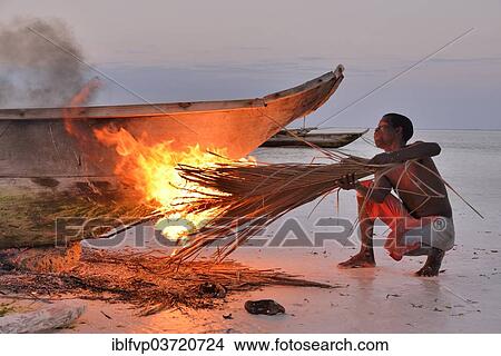 Picture - "Fisherman smoking his boat with burning palm fronds, to harden the surface and to remove vermin, Dongwe Beach, Dongwe, Zanzibar, Tanzania, Africa". Fotosearch