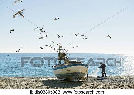 Stock Image - "Fisherman with a fishing boat on the beach of Noli, Riviera di Ponente, Liguria, Italy, Europe". Fotosearch