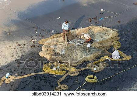 Stock Image - "Fishermen inspecting fishing nets on the beach, Varkala, Kerala, India, Asia". Fotosearch