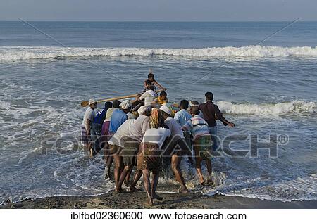 Stock Image - "Fishermen pushing a boot into the sea at the coast near Varkala, India, Asia". Fotosearch