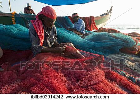 Stock Image - "Fishermen repairing fishing nets on the beach, Varkala, Kerala, India, Asia". Fotosearch