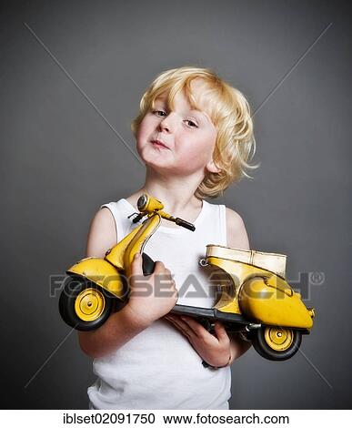 Stock Image - "Five-year-old boy holding a toy Vespa scooter, gift, happy face". Fotosearch