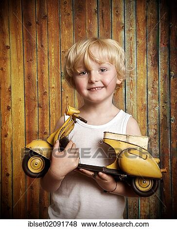 Stock Photo - "Five-year-old boy holding a toy Vespa scooter, gift, happy face". Fotosearch