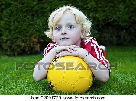 Stock Image - "Five-year-old boy wearing a FC Bayern Munich soccer dress, lying on the ground with a yellow soccer ball". Fotosearch