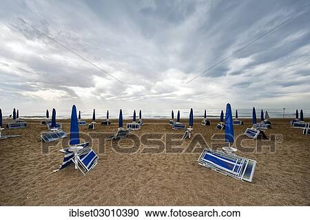 "Folded deck chairs and parasols on a beach by the sea with rain clouds, Cavallino, Jesolo, Venedig, Italy, Europe" View Large Photo Image Stock Image - "Folded deck chairs and parasols on a beach by the sea with rain clouds, Cavallino, Jesolo, Venedig, Italy, Europe". Fotosearch
