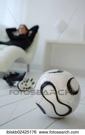 Football in front of a man on a couch in a bright living room View Large Photo Image Stock Photograph - Football in front of a man on a couch in a bright living room. Fotosearch