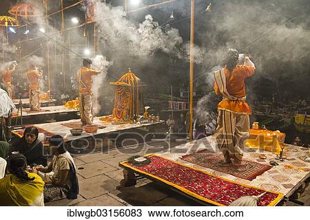 Stock Image - "Four Brahmins swinging incense burners during a puja ceremony on platforms at the shore in honour of the Mother Goddess Ganga, Hindu prayer ceremony, Varanasi, Uttar Pradesh, India, Asia". Fotosearch
