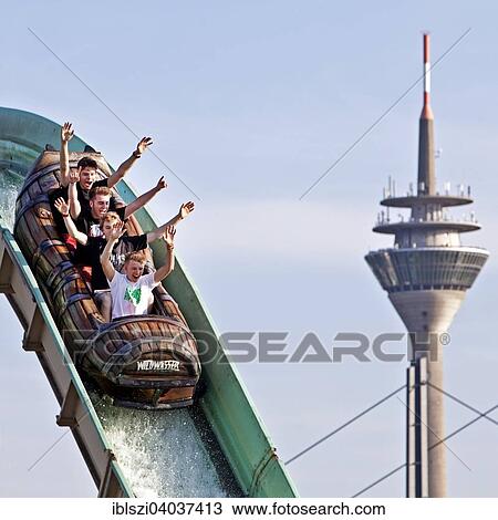 Stock Image - "Four young men on the log flume in front of the Rhine Tower, Dusseldorf, North Rhine-Westphalia, Germany, Europe". Fotosearch