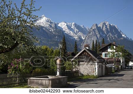 Stock Image - "Fruehlingsstrasse, a road with old houses and a fountain, Wetterstein Range, Alpspitze Mountain, Zugspitze Mountain, Garmisch-Partenkirchen, Upper Bavaria, Bavaria, Germany, Europe". Fotosearch
