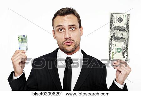 Stock Image - "Frustrated young man wearing a suit holding a small 100 euro banknote and a large 100 dollar bill, Austria, Europe". Fotosearch