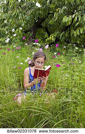 Stock Photo - "Girl, 11 years, reading a book sitting in a flower meadow". Fotosearch