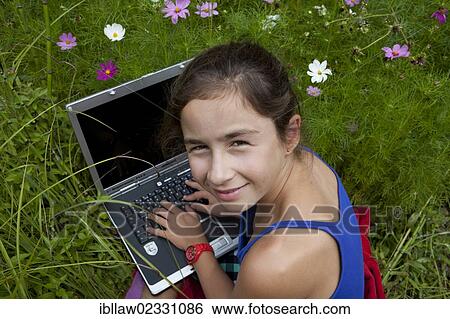 Stock Photograph - "Girl, 11 years, working on a laptop computer, notebook, sitting in a flower meadow". Fotosearch