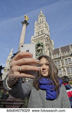 Stock Photo - "Girl, 14 years, taking a selfie in front of the Marian Column in Marienplatz square, New Town Hall, Munich, Upper Bavaria, Bavaria, Germany, Europe". Fotosearch