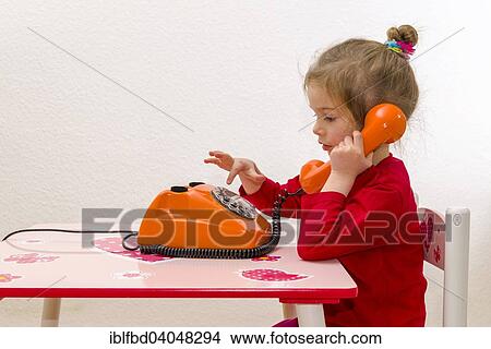 Picture - "Girl, 3 years, sitting at a table and using an orange telephone". Fotosearch