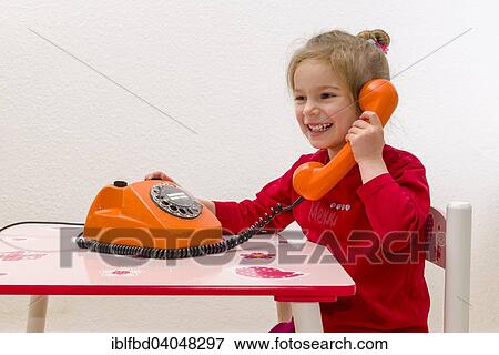 "Girl, 3 years, sitting at a table and using an orange telephone" View Large Photo Image Stock Photo - "Girl, 3 years, sitting at a table and using an orange telephone". Fotosearch